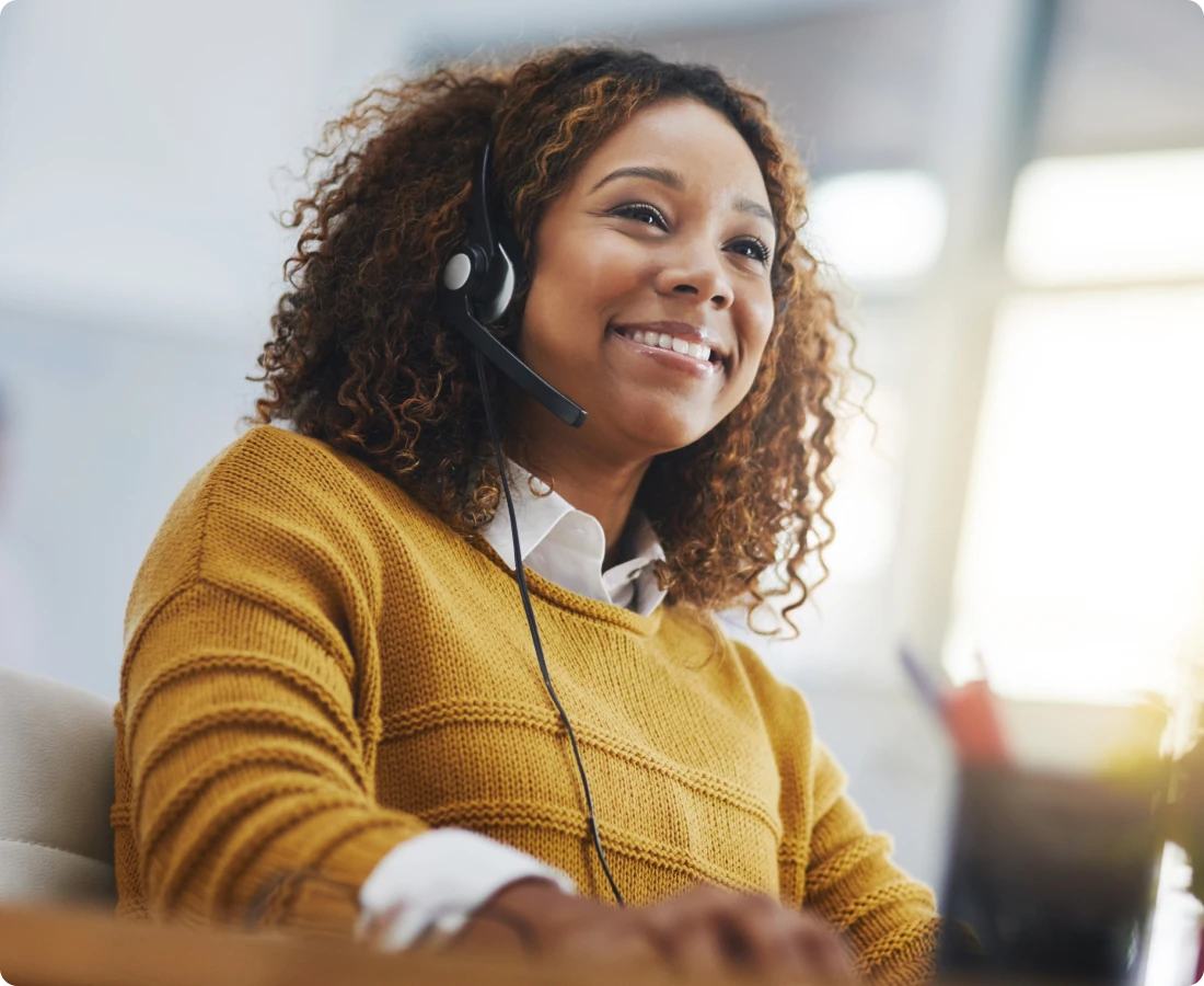 Woman in a yellow sweater wearing a headset speaking with a technology partner.