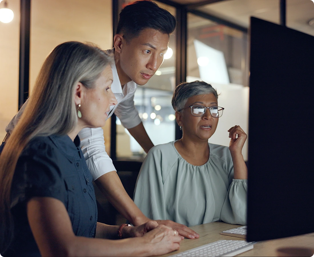 Three people gather around a desktop computer.